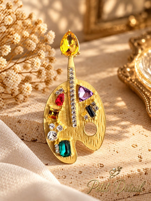 Jeweled artist palette brooch with multicolor crystals styled on a warm neutral background