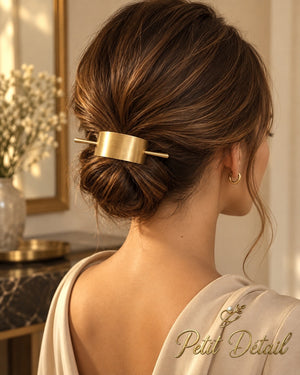 Woman wearing brushed gold-tone curved hair cuff secured with coordinating stick over a low bun