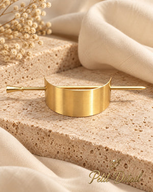 Curved brushed gold-tone hair cuff and coordinating stick styled on beige stone with ivory fabric and white flowers