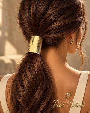 Woman wearing wide diagonal-textured gold-tone hair cuff over a low brown ponytail