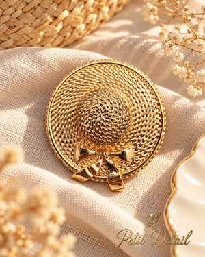Gold-tone woven sun hat brooch with bow styled on neutral fabric