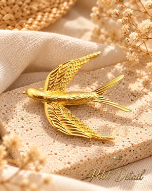 Gold-tone flying swallow brooch styled on neutral fabric