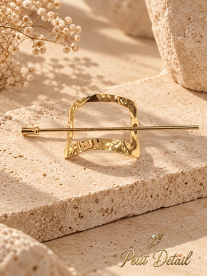 Hammered square gold hair cuff and coordinating stick displayed on beige stone with ivory flowers