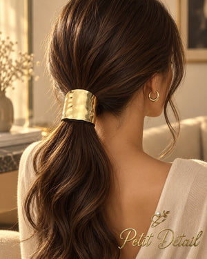 Woman wearing wide hammered gold-tone hair cuff around a low brown ponytail