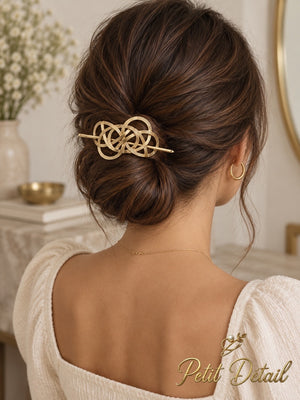 Woman wearing interwoven gold-tone hair cuff secured with matching stick on a low bun