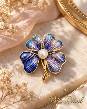 Midnight-blue glitter clover brooch with pearl-look center displayed on cream stone with blush satin and delicate white flowers