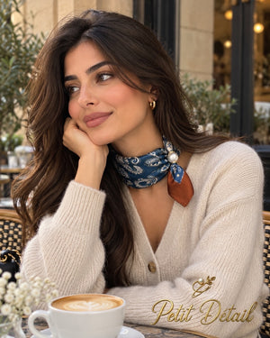 Woman wearing navy paisley magnetic scarf with cream pattern, rust accent tail and pearl magnetic closure