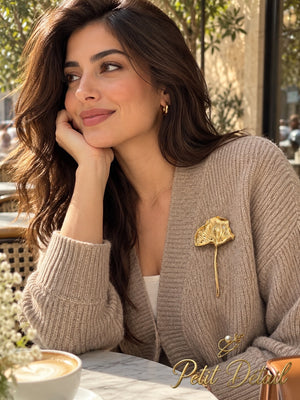 Woman wearing long-stem gold-tone ginkgo leaf brooch on a beige knit cardigan