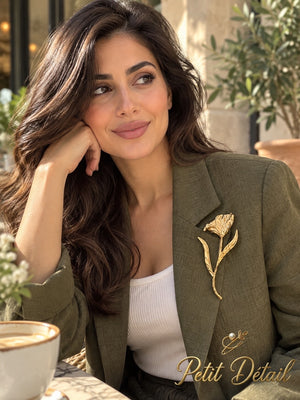 Woman wearing a long-stem sculpted gold-tone flower brooch on an olive-green blazer