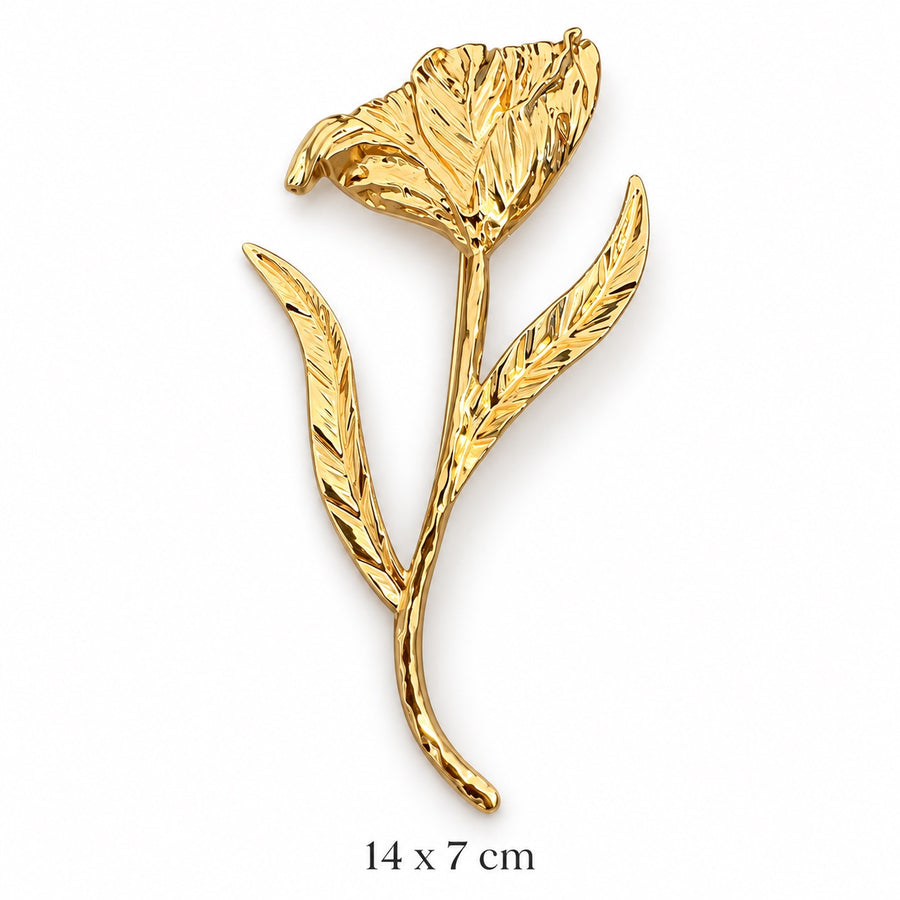 Sculpted gold-tone open bloom brooch with textured flower, two veined leaves and flowing long stem on white background, 14 × 7 cm