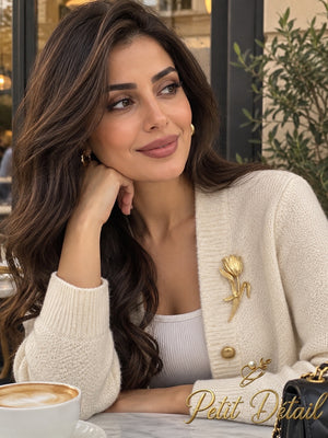 Woman wearing a sculpted gold-tone tulip brooch on a cream cardigan