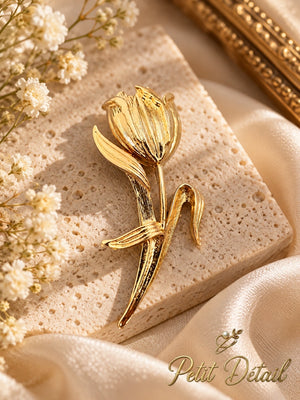 Polished textured gold-tone tulip flower brooch on light beige stone beside cream satin and tiny white flowers
