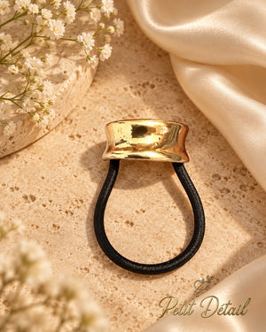 Small polished hourglass gold-tone hair cuff with black elastic styled on beige stone and ivory satin