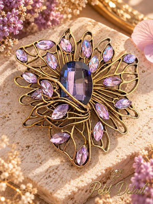 Violet crystal-look filigree bloom brooch styled on beige travertine with soft purple blossoms